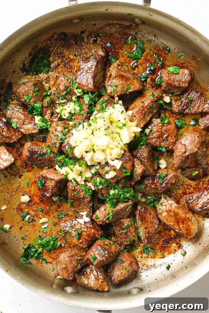 Sizzling Garlic Herb Steak Bites 5 Garlic and fresh herbs being added to the pan with seared steak bites, ready to be tossed.