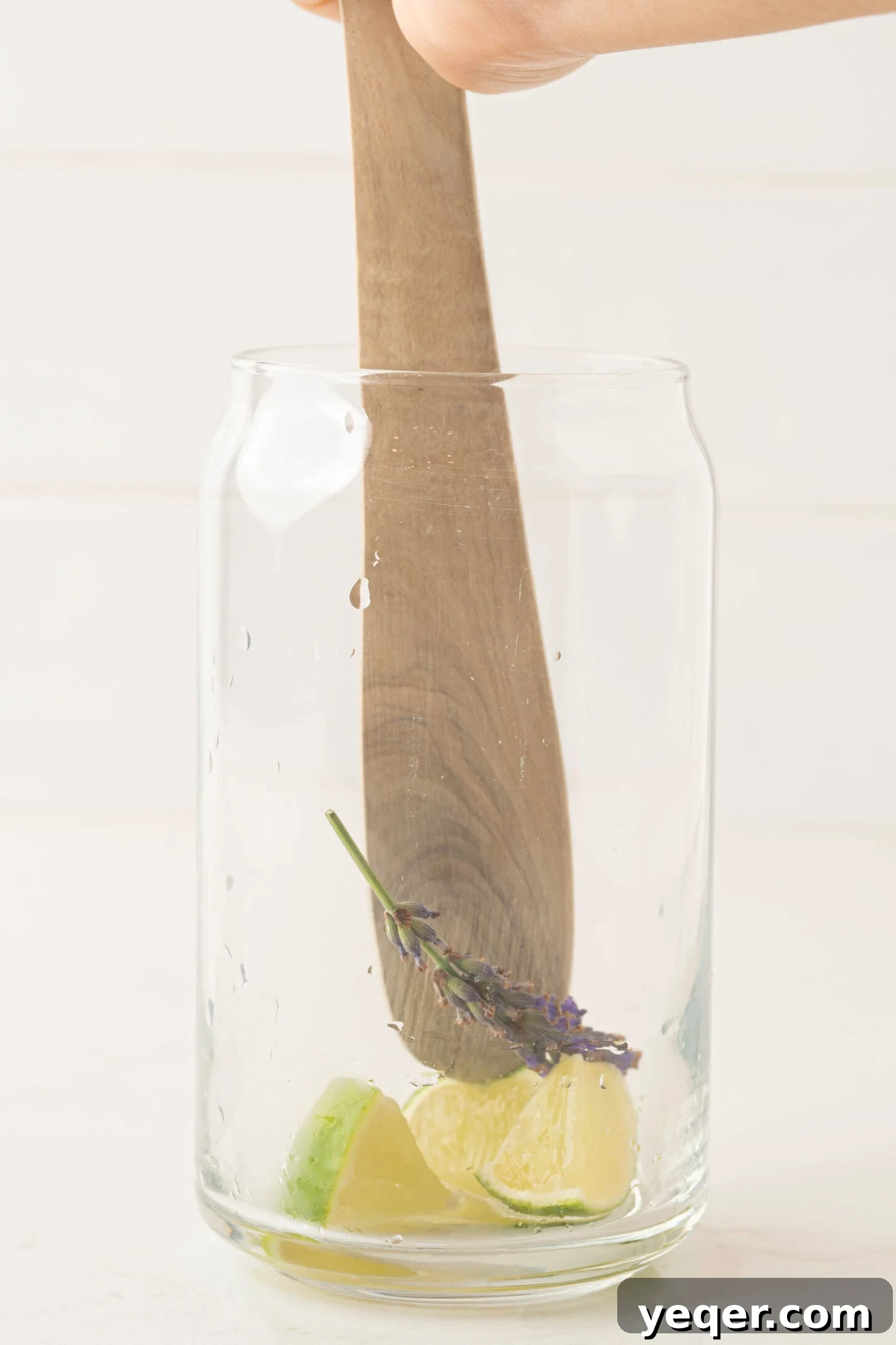 Indigo Bloom Delight 5 Fresh lime wedges and lavender sprigs being muddled in a glass, releasing their aromatic oils.