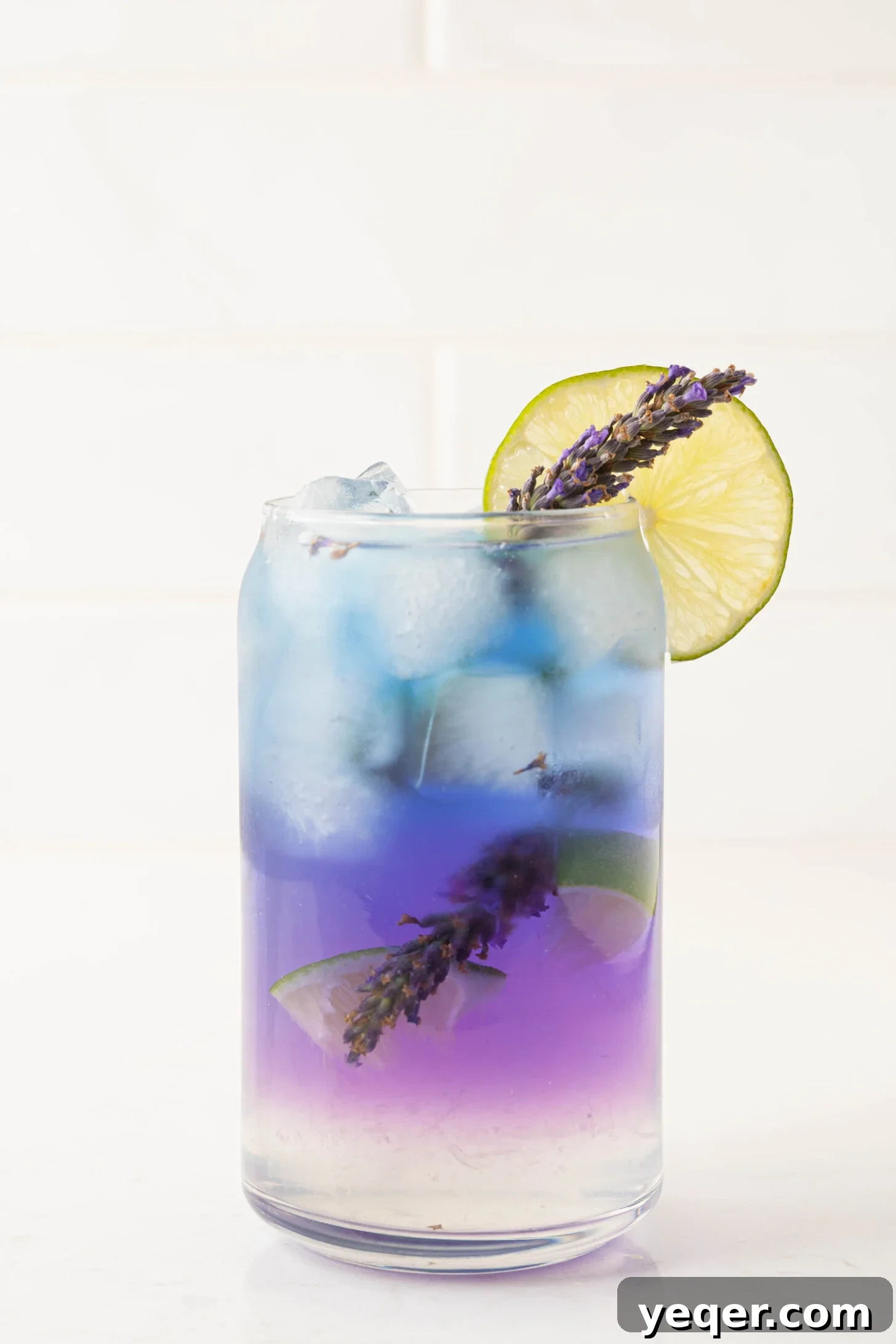Indigo Bloom Delight 10 A beautifully crafted butterfly pea flower cocktail with a vibrant purple gradient, garnished with a lime slice and a lavender sprig.