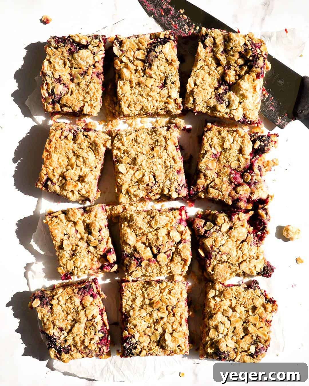 Twelve neatly cut gluten-free blackberry crumb bars arranged enticingly on a rustic wooden platter, showcasing their distinct layers of golden crumble and rich, dark berry filling. A knife rests beside them, inviting guests to enjoy this exquisite dessert.