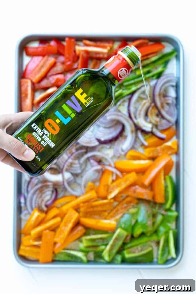 Effortless Sheet Pan Steak Fajitas 5 O-Live & Co. Robust olive oil being drizzled over a sheet pan of colorful peppers and onions.