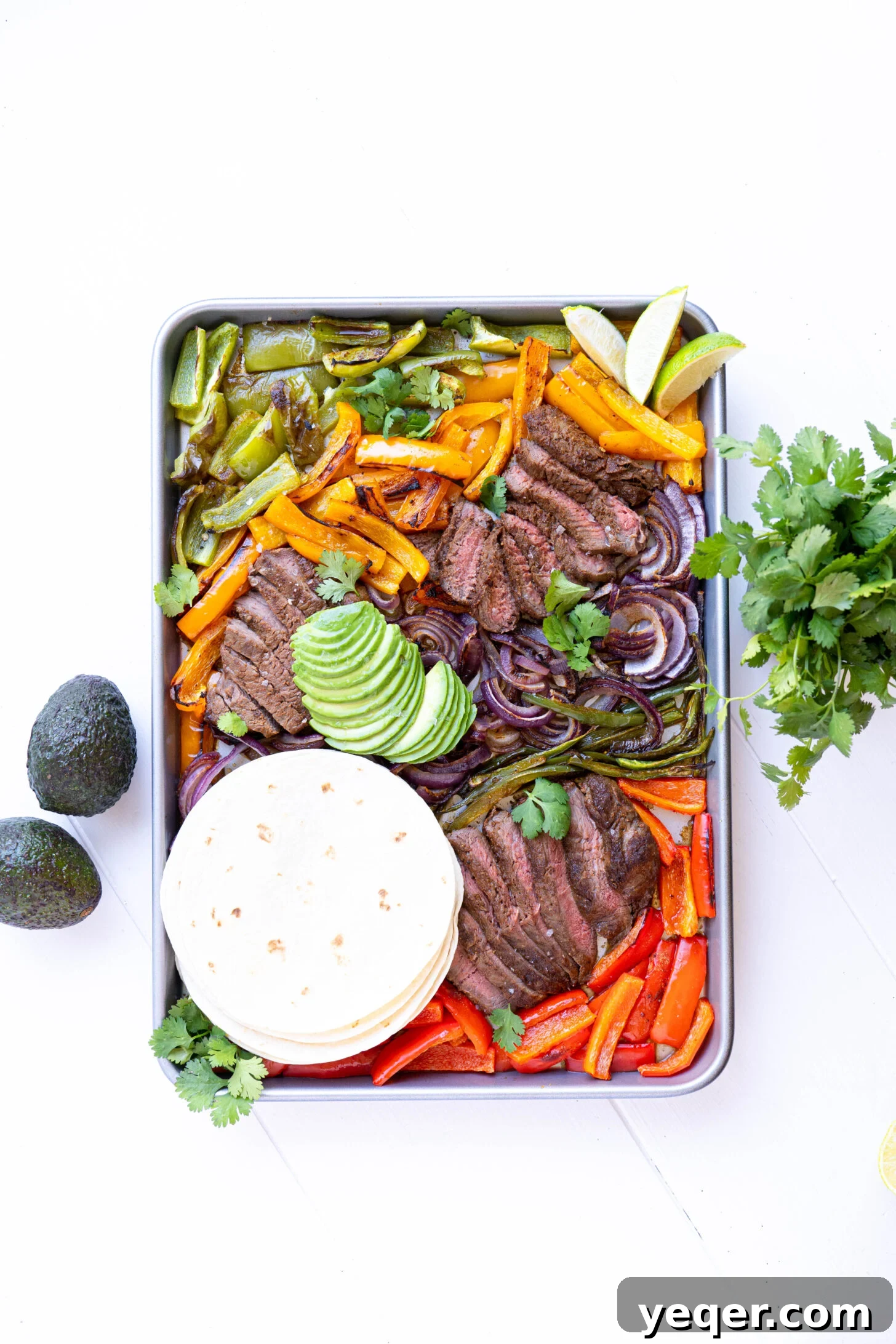 Effortless Sheet Pan Steak Fajitas 7 A sheet pan generously loaded with beautifully cooked steak, blistered bell peppers, and caramelized onions, garnished with fresh cilantro and lime wedges.