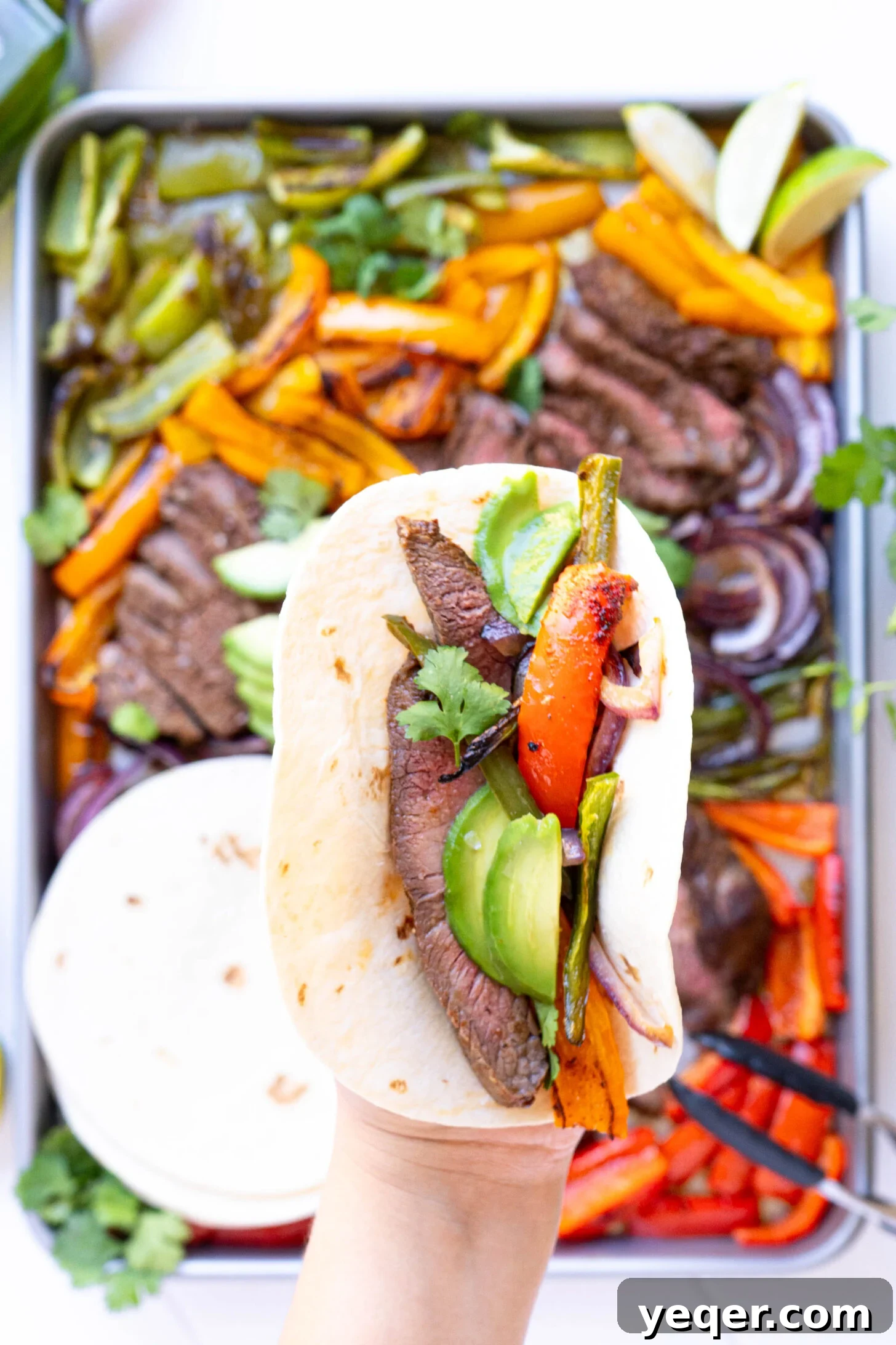 Effortless Sheet Pan Steak Fajitas 8 A hand reaching for a delicious steak fajita, highlighting the tender meat and vibrant vegetables on a sheet pan.