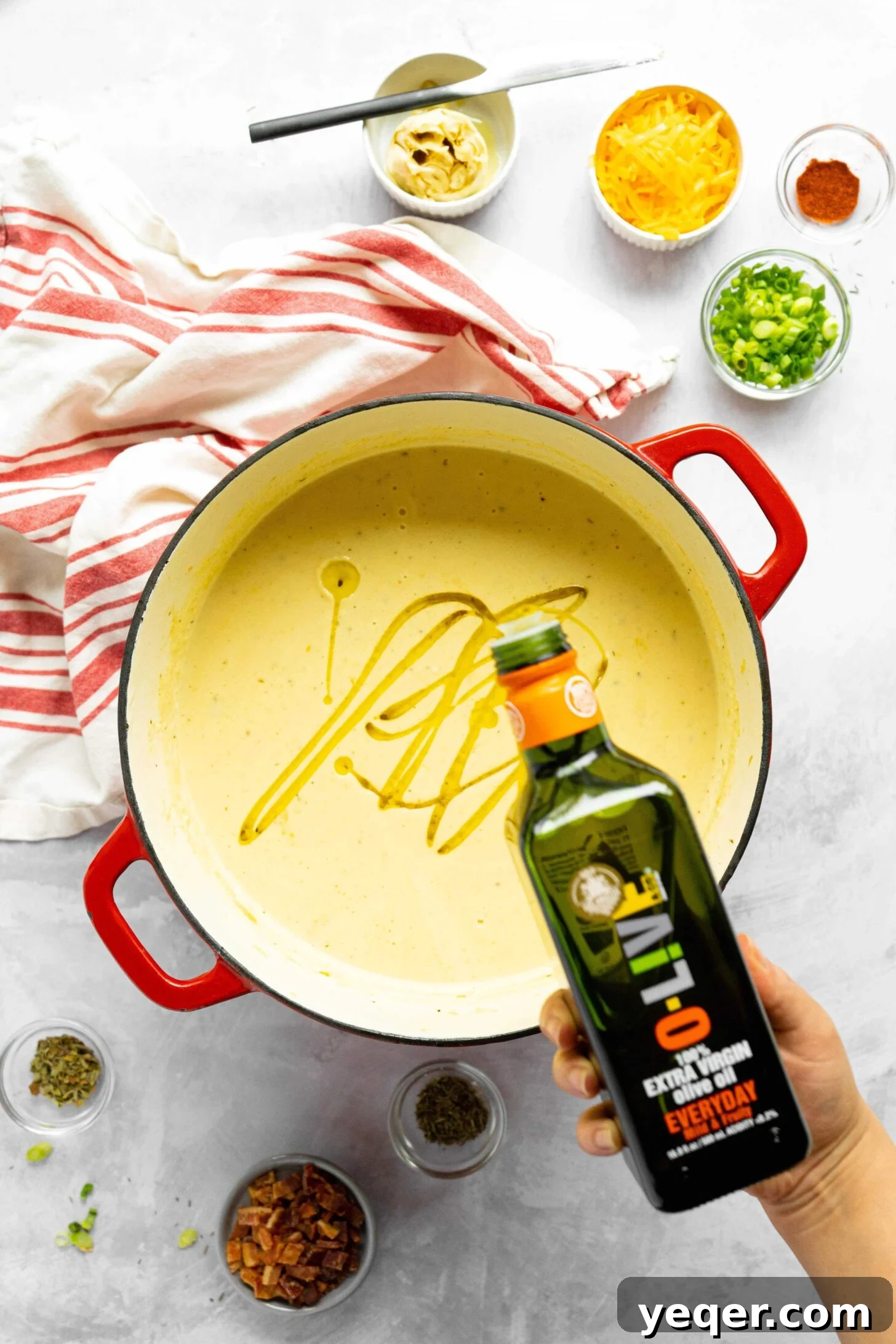 Decadent Loaded Cauliflower Dream 5 A hand drizzling golden olive oil into a pot of creamy cauliflower soup, creating beautiful ripples on the surface.