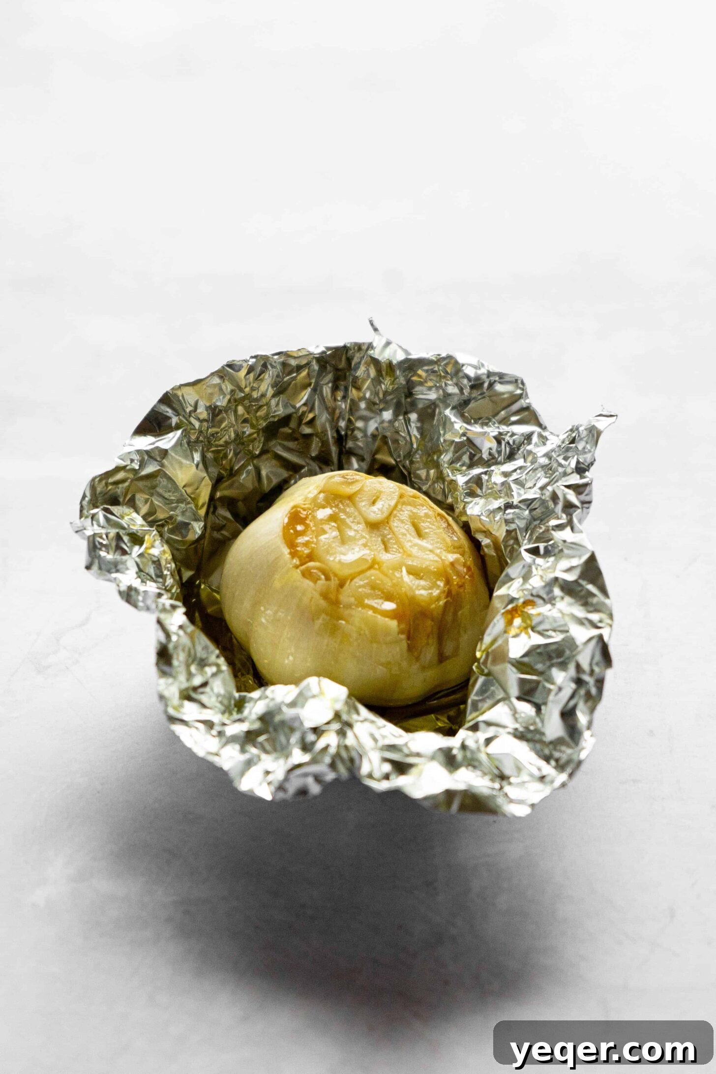 Decadent Loaded Cauliflower Dream 6 An aluminum foil pouch containing a head of roasted garlic drizzled with olive oil, on a baking sheet.