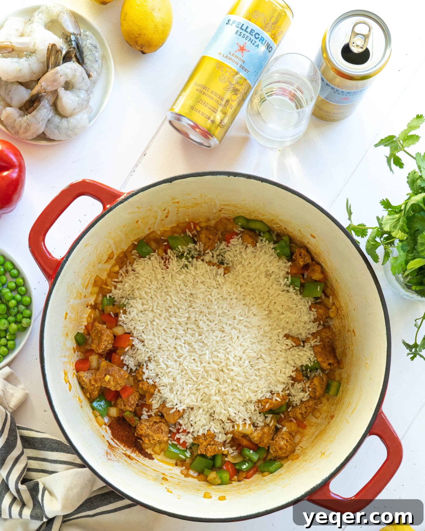 Golden Saffron Shrimp Paella 5 A pot on a white table with rice, chorizo and veggies next to cans of S.Pellegrino