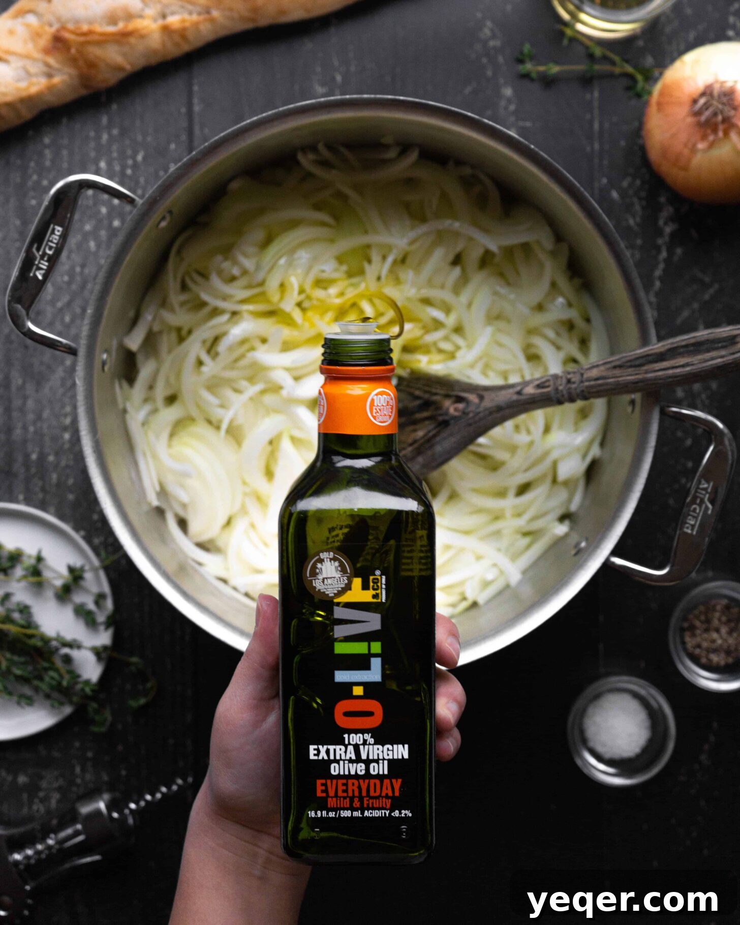 Homemade French Onion Soup Elevated with O-Live and Co 3 A hand pouring olive oil into a pot full of onions