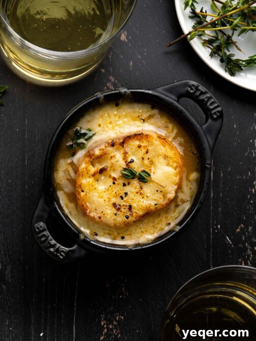 A bowl of French Onion Soup next to glasses of wine