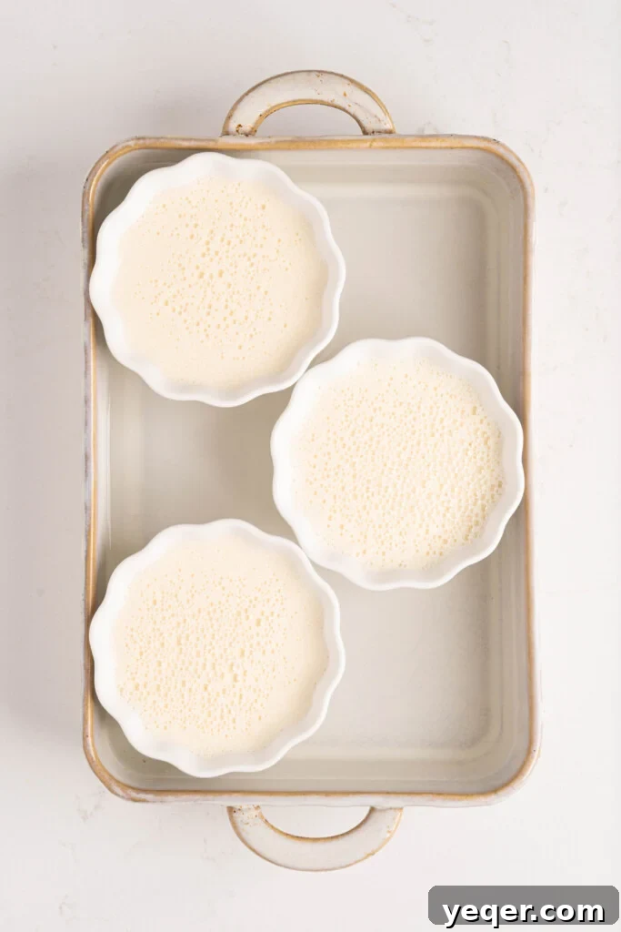 Silky Puerto Rican Caramel Flan 9 Multiple individual flans baking gently in a water bath within a large roasting pan.
