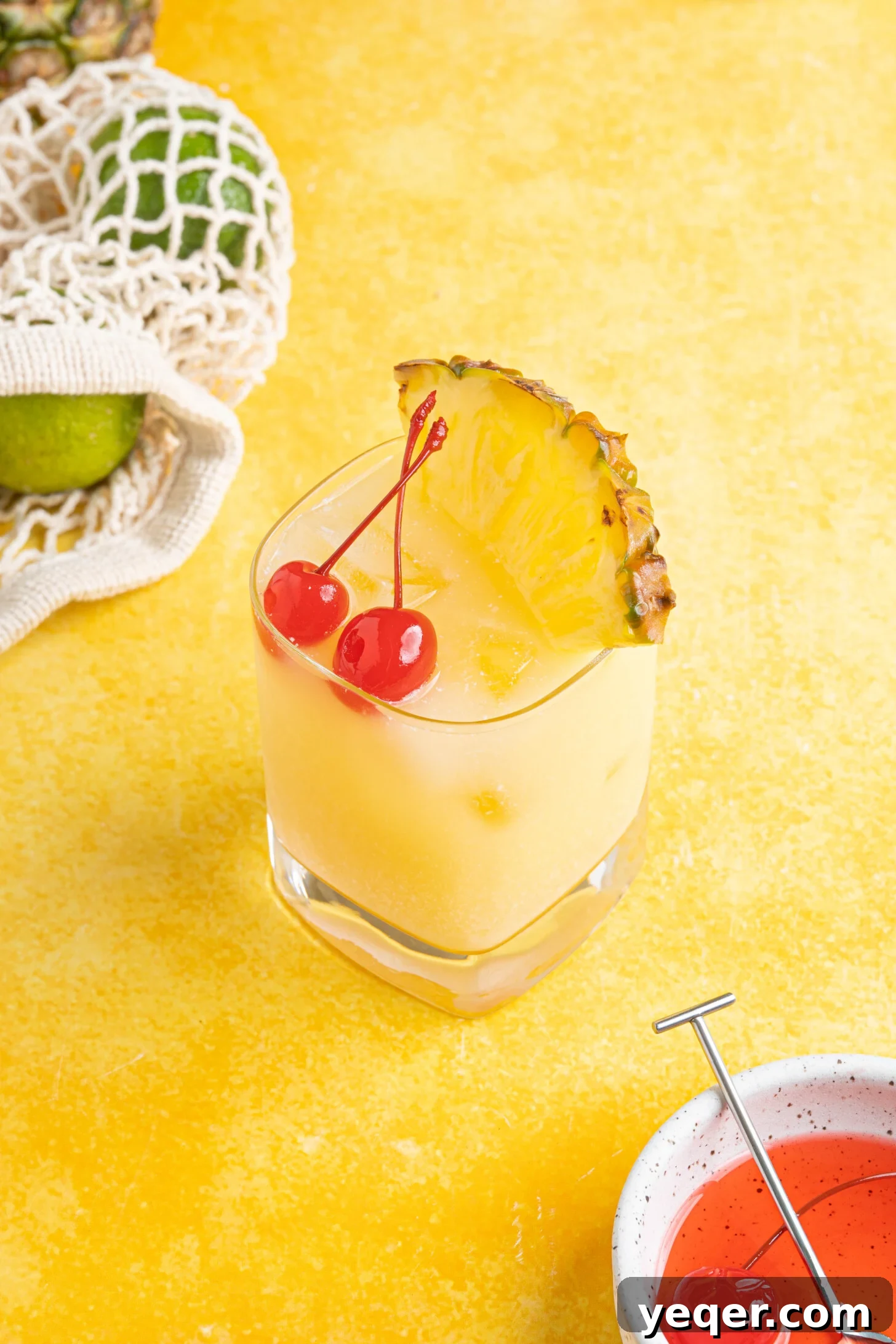 Arctic Tropics 2 A refreshing Pina Colada on the rocks cocktail garnished with a slice of pineapple and a cherry, sitting on a yellow counter, ready to be enjoyed.