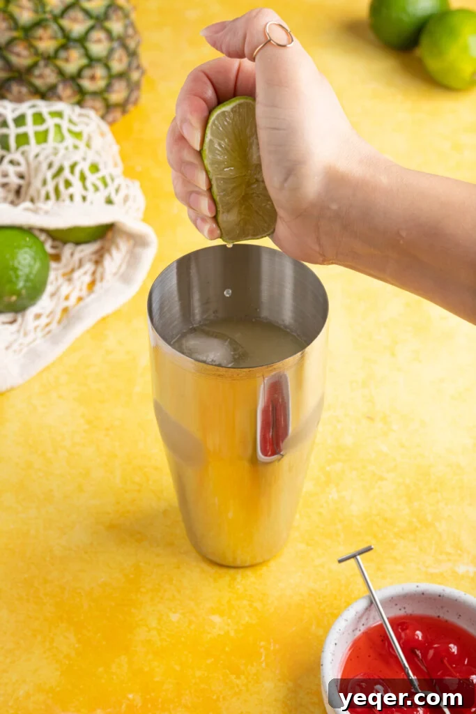 Arctic Tropics 4 A hand squeezing a fresh lime wedge directly into a cocktail shaker filled with ice and other ingredients, demonstrating the preparation of a Pina Colada on the Rocks.