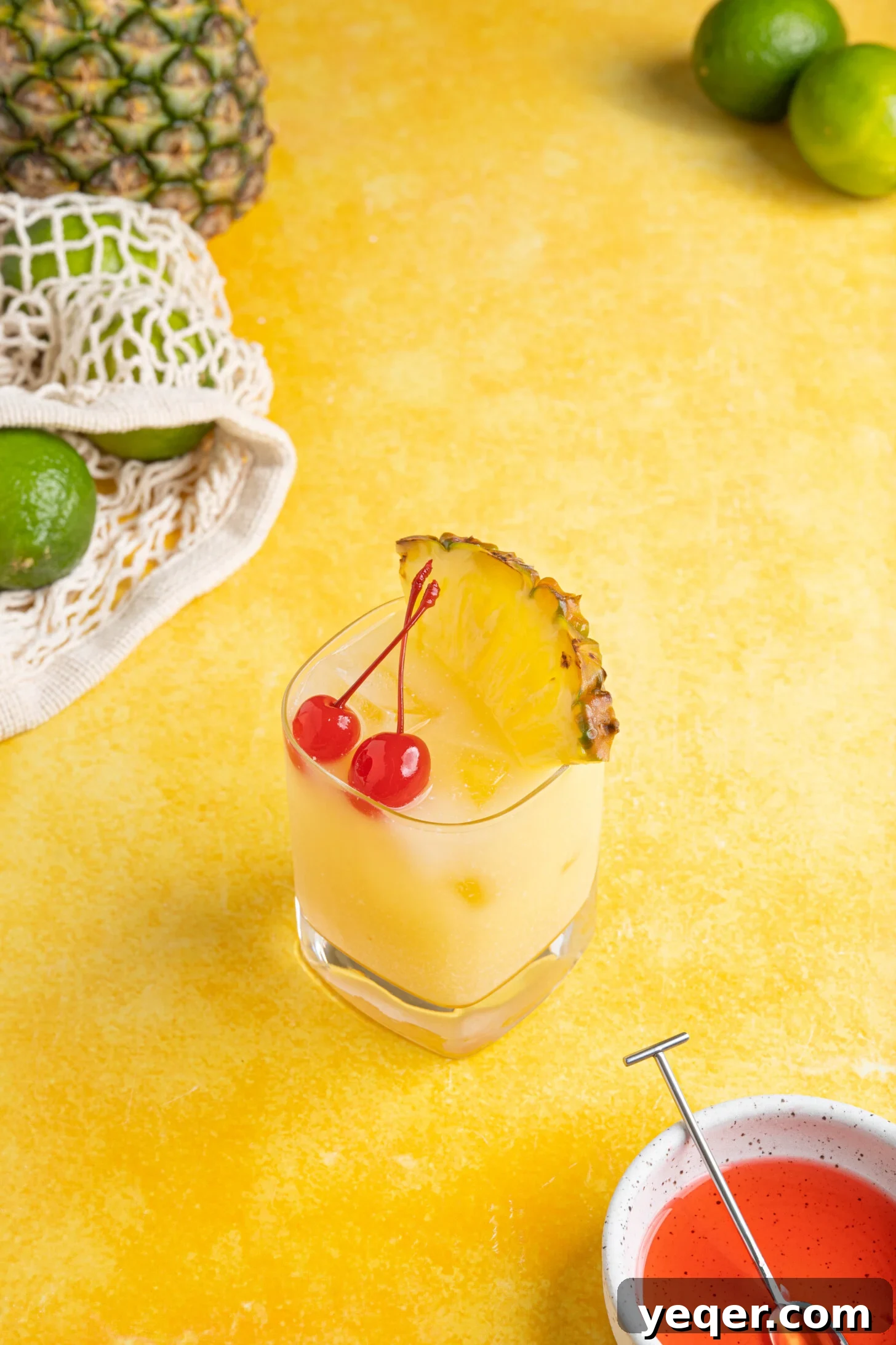 Arctic Tropics 6 A beautifully presented Pina Colada on the rocks cocktail, garnished with a pineapple wedge and a maraschino cherry, set against a vibrant yellow background.