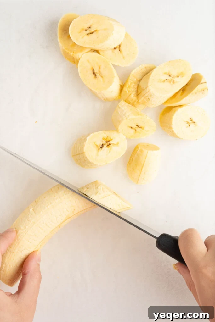 Caramelized Golden Plantains 6 A peeled plantain being sliced diagonally into thick pieces.