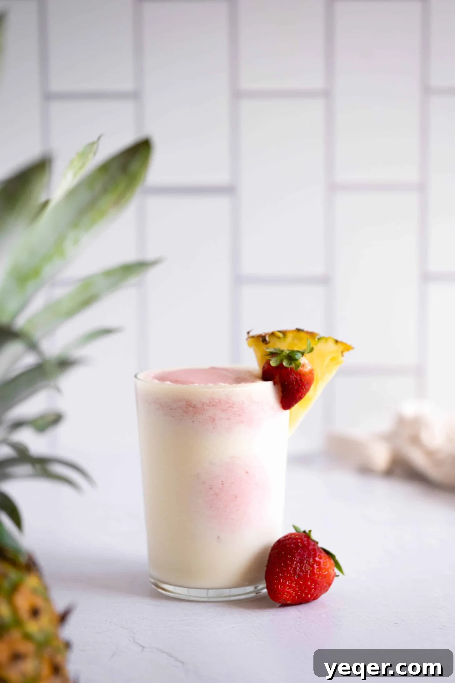 Pink Pina Perfection 2 A vibrant red and white layered strawberry pina colada in a tall glass, garnished with a fresh strawberry and a pineapple wedge. The drink looks frosty and incredibly refreshing, set against a bright, summery background.