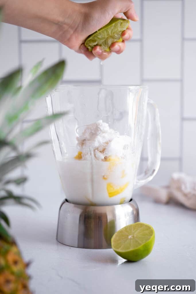 Pink Pina Perfection 5 A fresh lime half being expertly squeezed over the blender opening, allowing its zesty, aromatic juice to infuse the Piña Colada mixture with a refreshing citrus note.