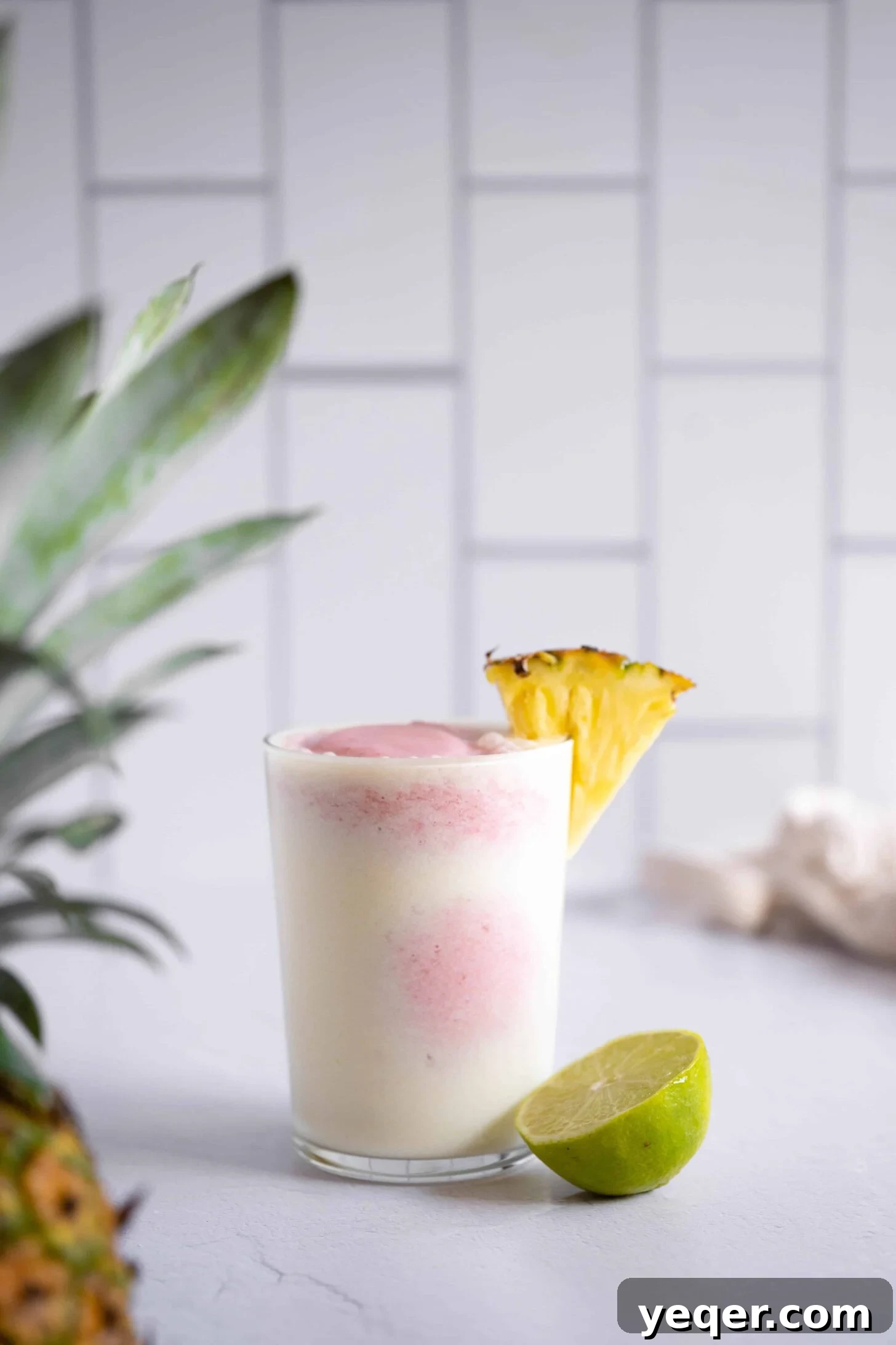 Pink Pina Perfection 8 Another enticing close-up shot of a beautifully layered strawberry pina colada in a clear glass, distinctly showcasing the separated pink and white layers and its inviting, frosty texture. A fresh strawberry garnish sits on the rim.