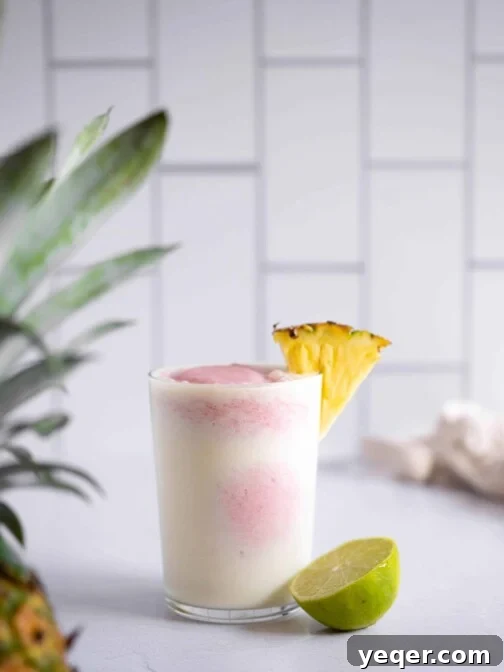A vibrant strawberry pina colada in a glass, with distinct layers of pink and white, garnished with a fresh strawberry.