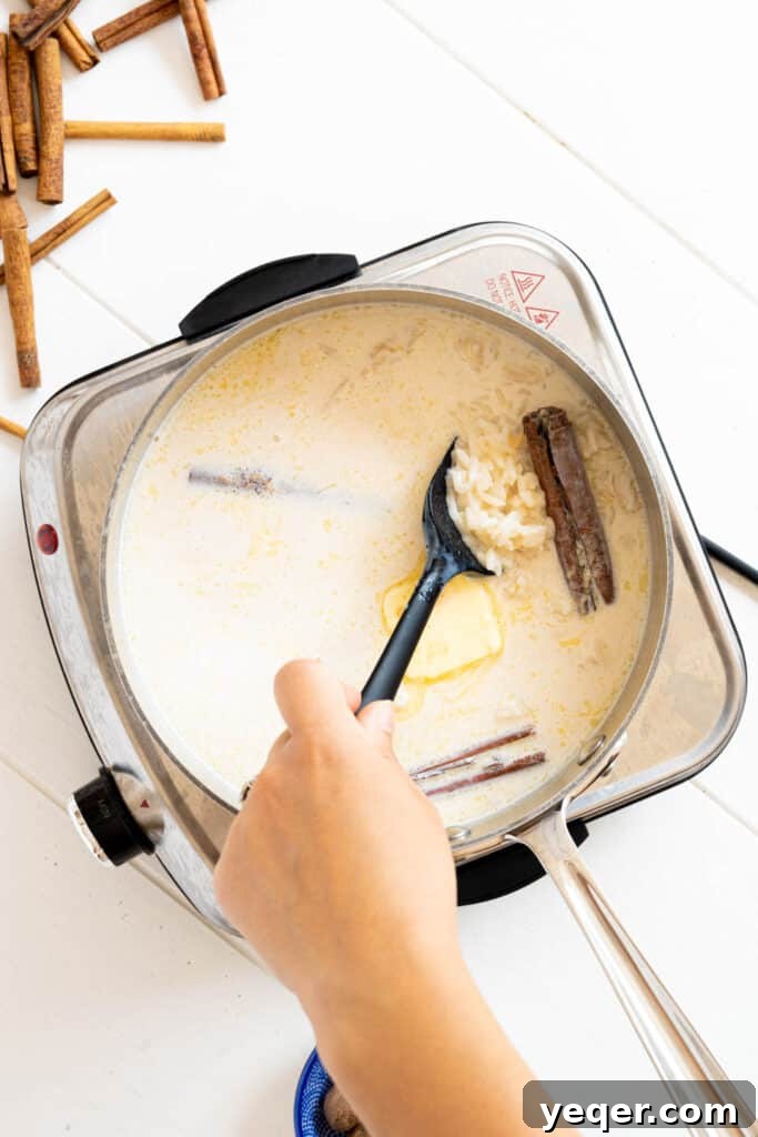 Velvety Rice Dream 5 A hand stirring a pot of Arroz con Leche with a spoon, showing whole milk, brown sugar, and butter being incorporated into the partially cooked rice and spices.