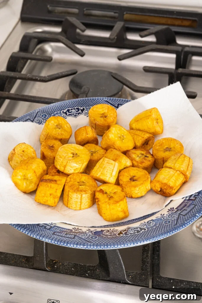 25 Dakikada Geleneksel Porto Riko Mofongosu 7 Crispy, golden-fried plantains resting on a paper towel-lined plate, absorbing excess oil.