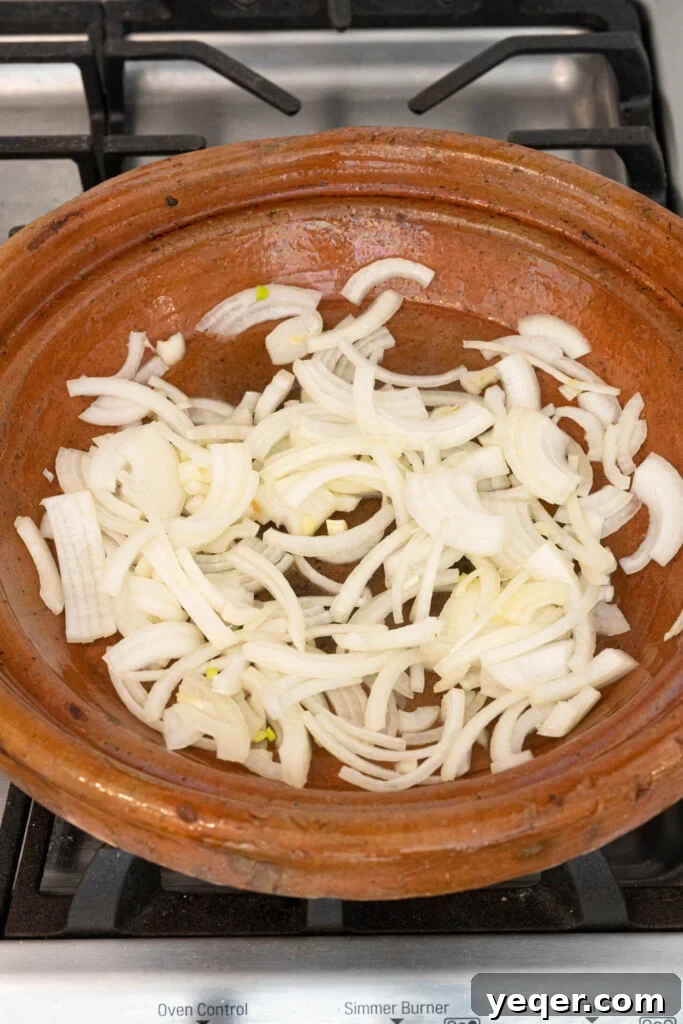 Spiced Moroccan Potato and Vegetable Tagine 9 Sliced onions gently sautéing in shimmering olive oil at the bottom of a traditional tagine pot on a stovetop, gradually turning translucent and aromatic.