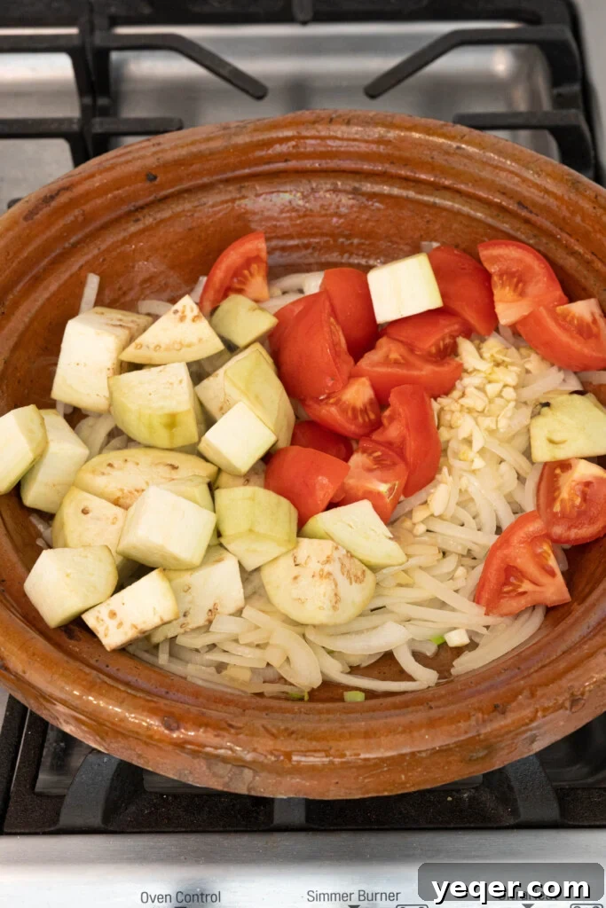 Spiced Moroccan Potato and Vegetable Tagine 10 A vibrant mix of sautéed onions, tomatoes, garlic, and eggplant forming a rich and aromatic base layer in a tagine pot, awaiting the addition of fresh vegetables.