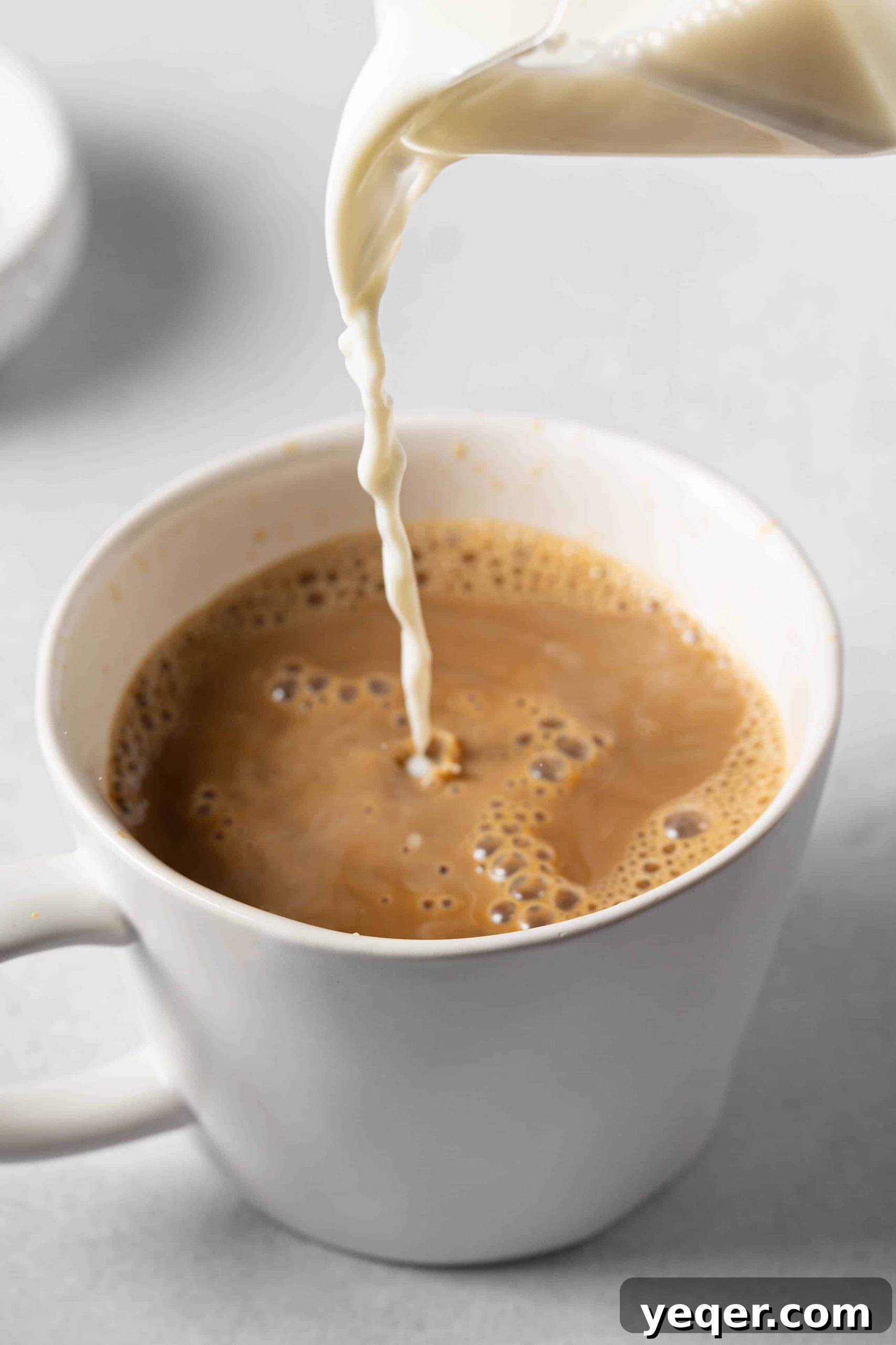 Milk being poured into a mug of coffee to create a beautiful Café con Leche.