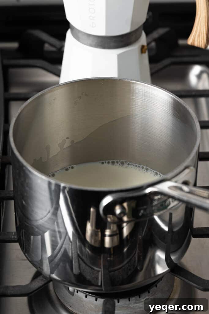 Milk warming in a small saucepan on a stovetop, essential for achieving the creamy texture of Café con Leche.