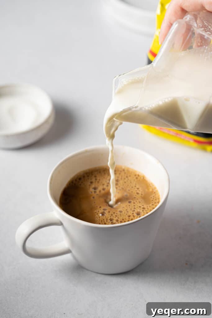Steamed milk being poured into a mug already containing coffee, completing the traditional Café con Leche.