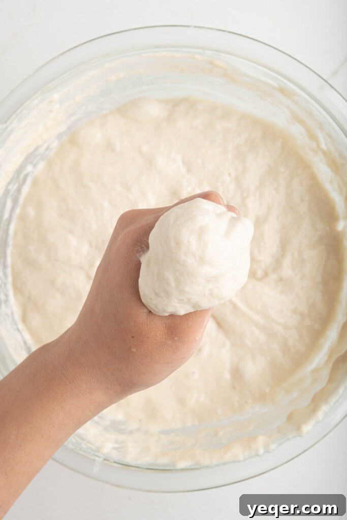 Sfenj: Moroccan Spongy Delights 6 A hand gently pulling a small ball of Moroccan donut dough from the main batch, preparing to shape it.