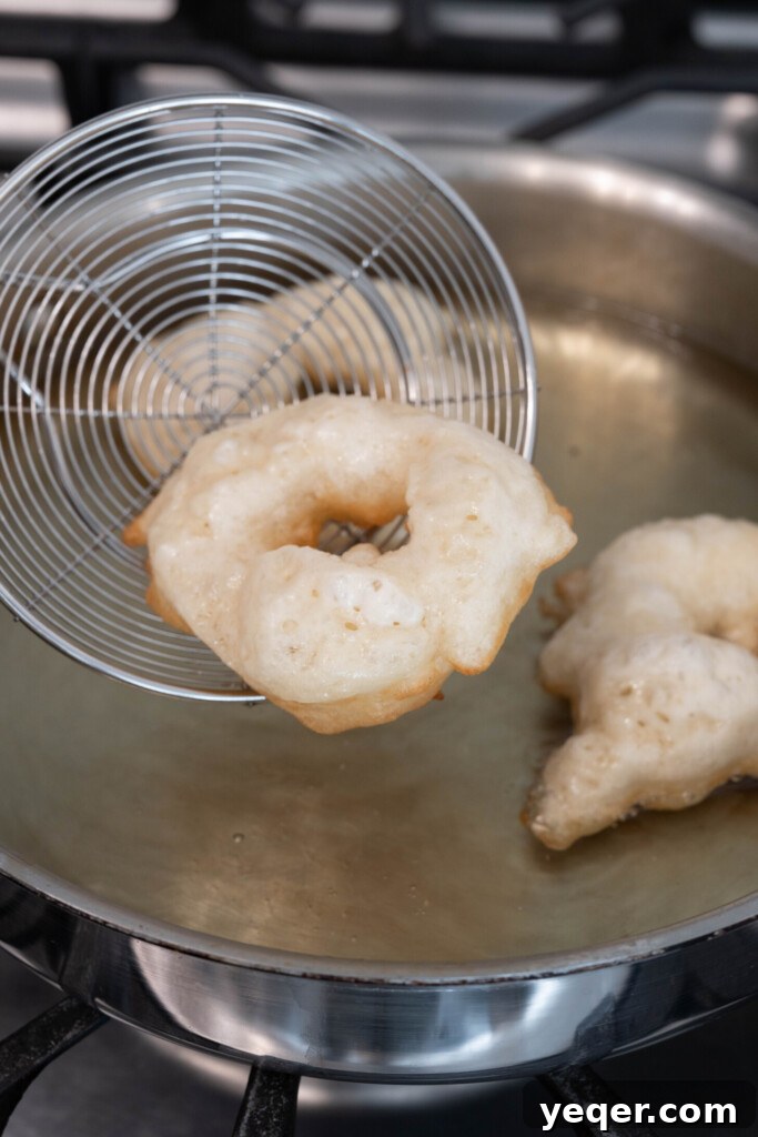 Sfenj: Moroccan Spongy Delights 8 Several Moroccan donuts sizzling and turning golden brown as they fry in hot oil within a pan.