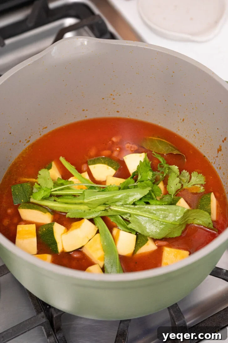 Hearty Puerto Rican Bean Stew 6 All the ingredients for Habichuelas Guisadas, including spices, tomato sauce, water, cubed squash, and canned beans, added to the simmering sofrito in a pot.