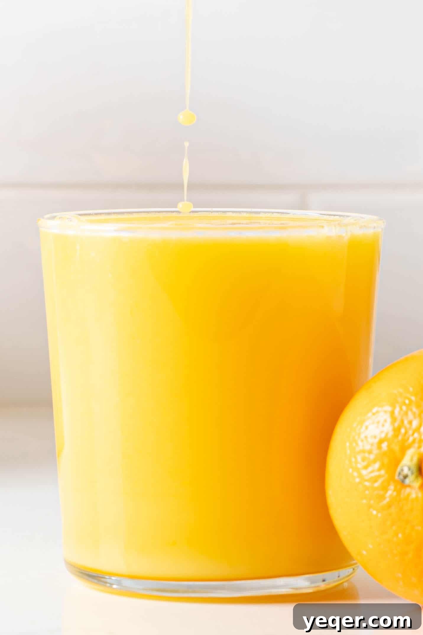 Hand-Pressed Orange Delight 10 A sparkling glass of fresh orange juice, garnished with an orange slice, sitting on a light-colored surface, inviting a refreshing sip.