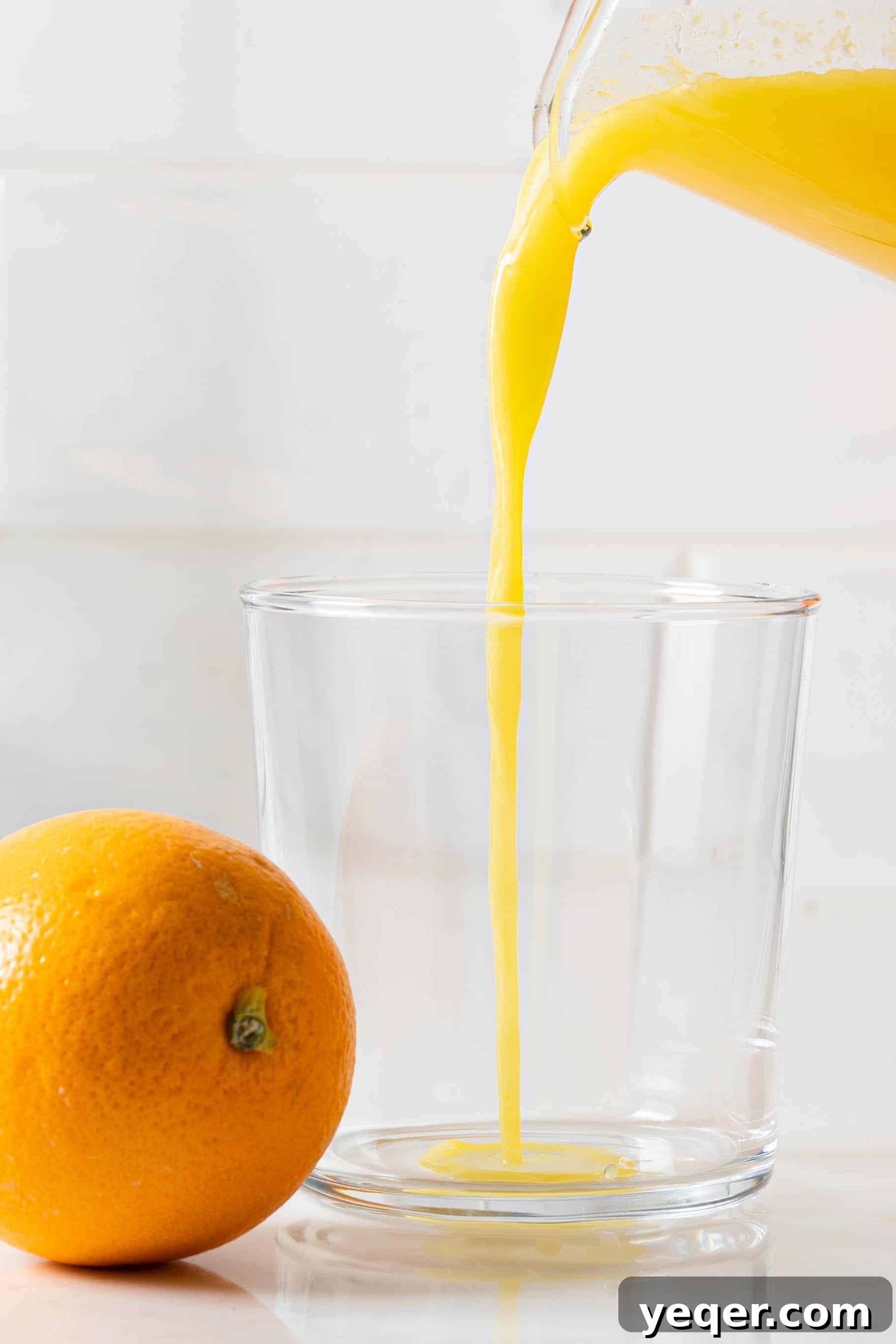 Hand-Pressed Orange Delight 4 Freshly squeezed orange juice is being poured from a pitcher into a tall glass, showcasing its vibrant color.