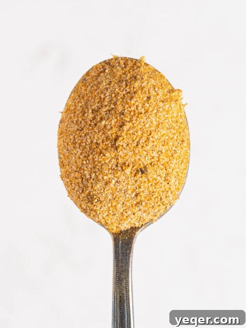 A close-up shot of homemade Adobo seasoning in a small bowl, with a spoon taking a scoop.