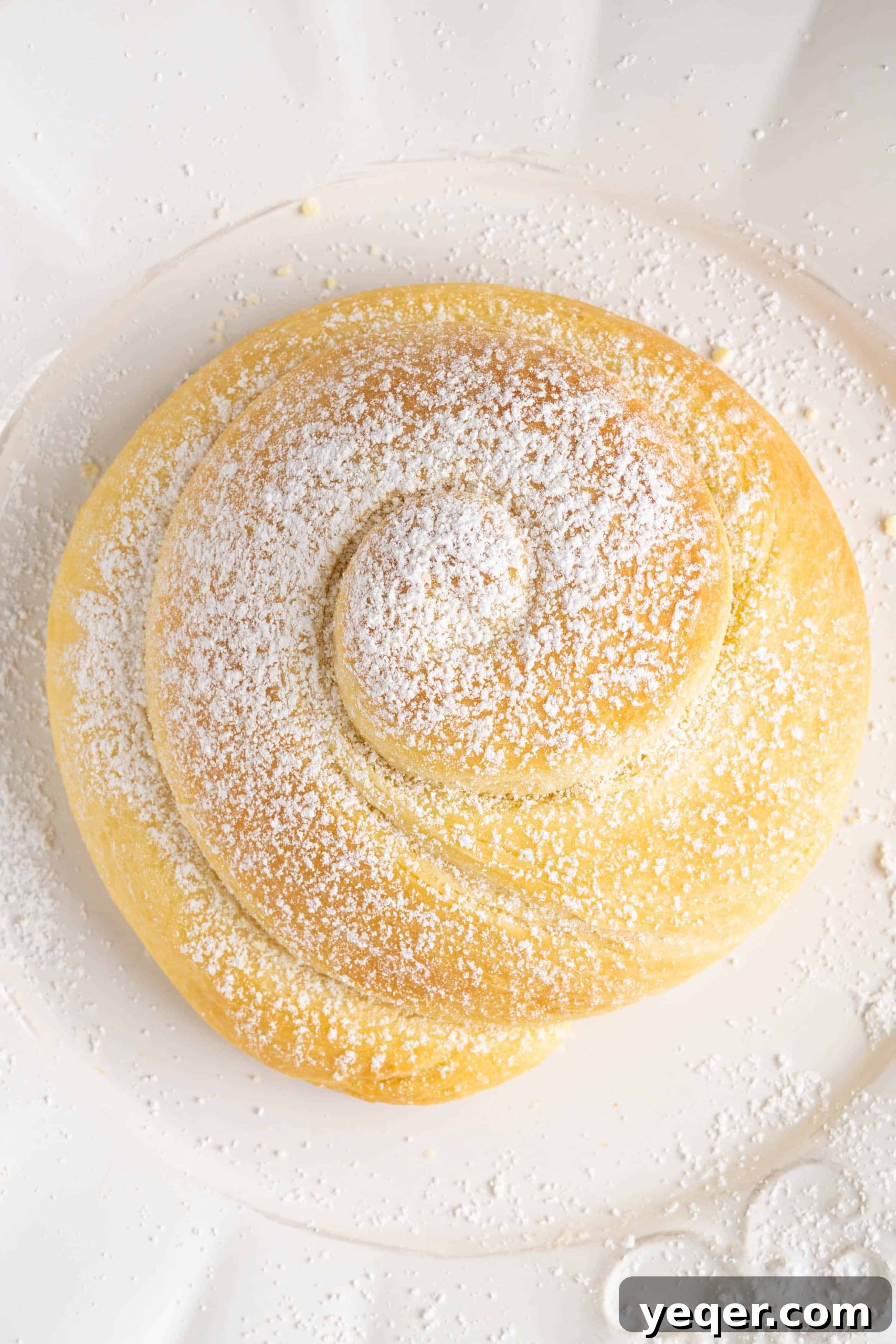 Golden Puerto Rican Sweet Mallorca 4 Three golden-brown Pan de Mallorca buns artfully arranged on a pristine white plate, garnished with a generous dusting of powdered sugar.