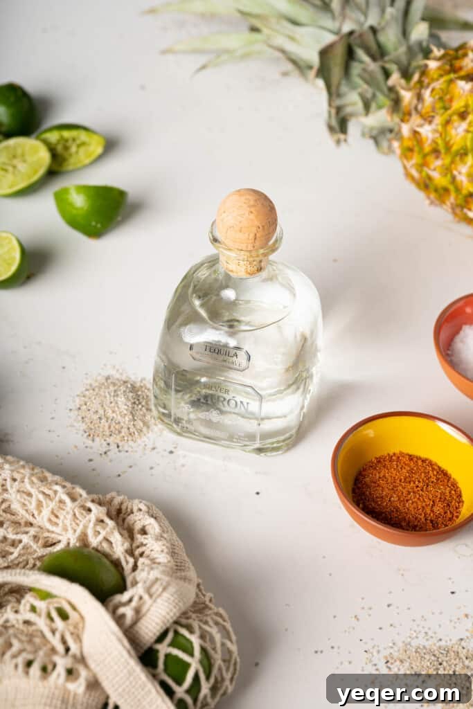 Pineapple Paradise Margarita 4 Ingredients for making margaritas, including a bottle of tequila, lime, and pineapple juice.
