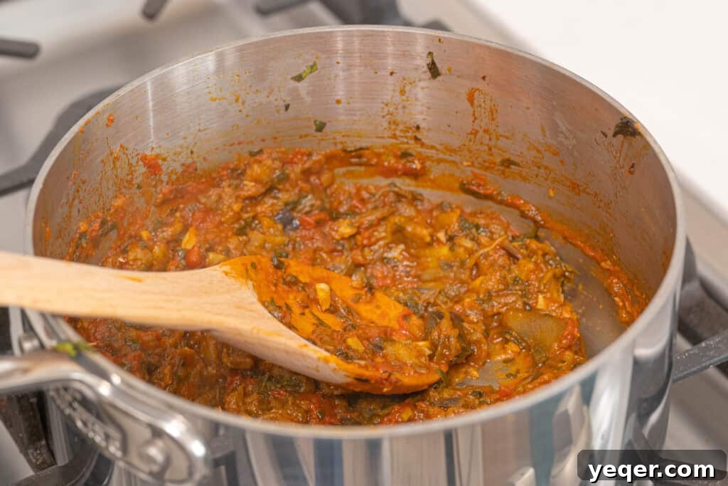 Zaalouk: Flavorful 30-Minute Moroccan Eggplant Dip 6 A close-up view of the cooked Zaalouk in the pot, being mashed with a fork to achieve the desired consistency, with steam gently rising.
