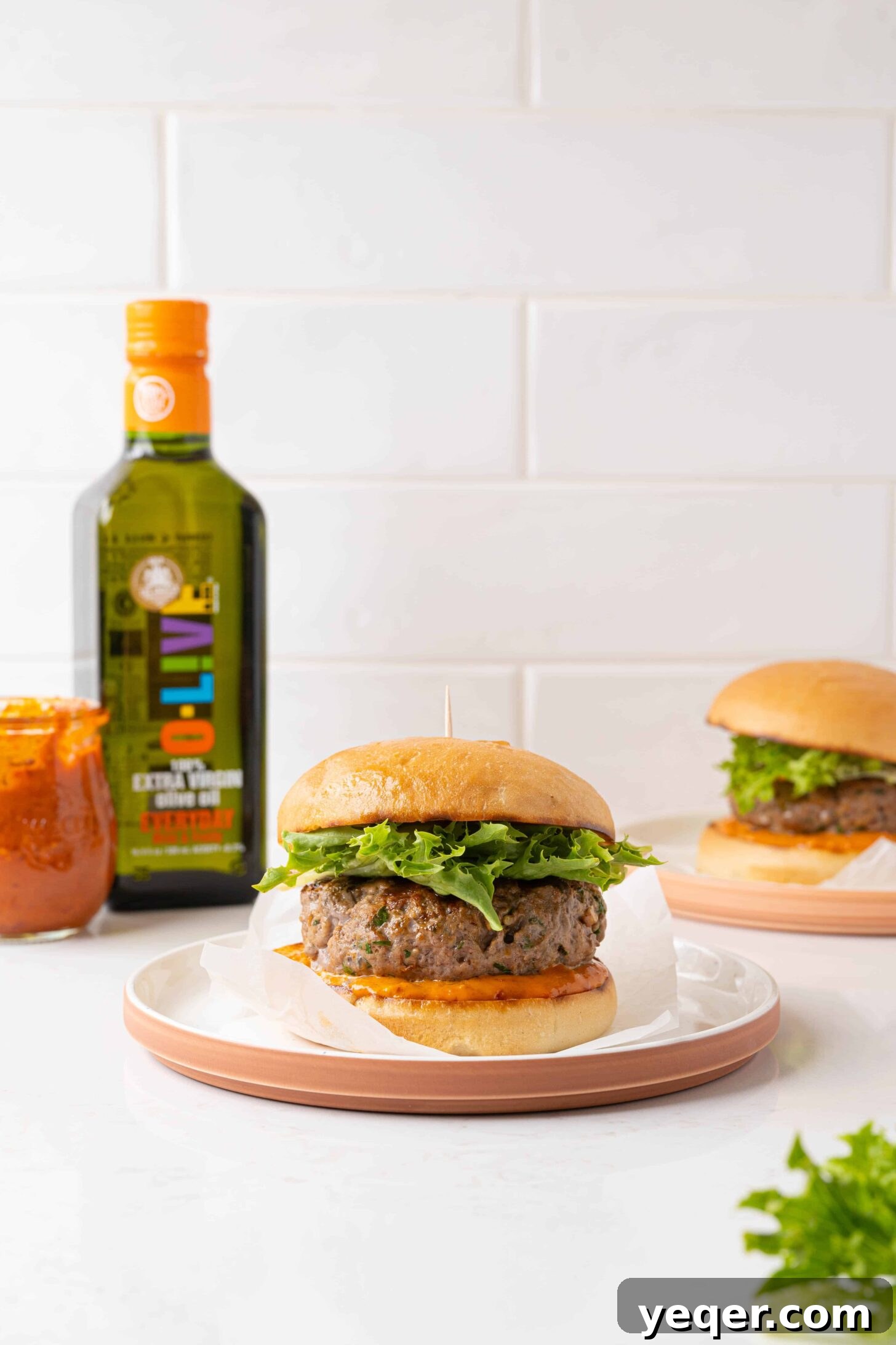 Spicy Harissa Burgers 2 A vibrant harissa lamb burger, perfectly grilled, served on a plate with fresh greens and a toasted bun, drizzled with O-Live & Co. olive oil.