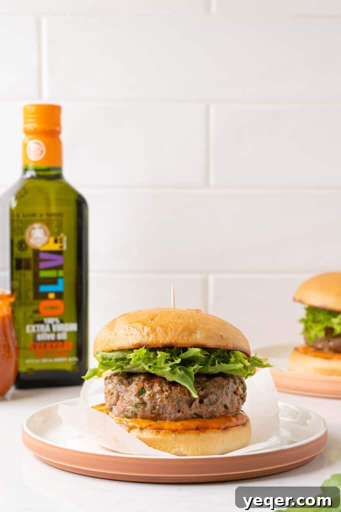 Spicy Harissa Burgers 6 A freshly assembled harissa lamb burger, complete with toasted bun, harissa mayo, mixed greens, and tomato slices, ready to be enjoyed.