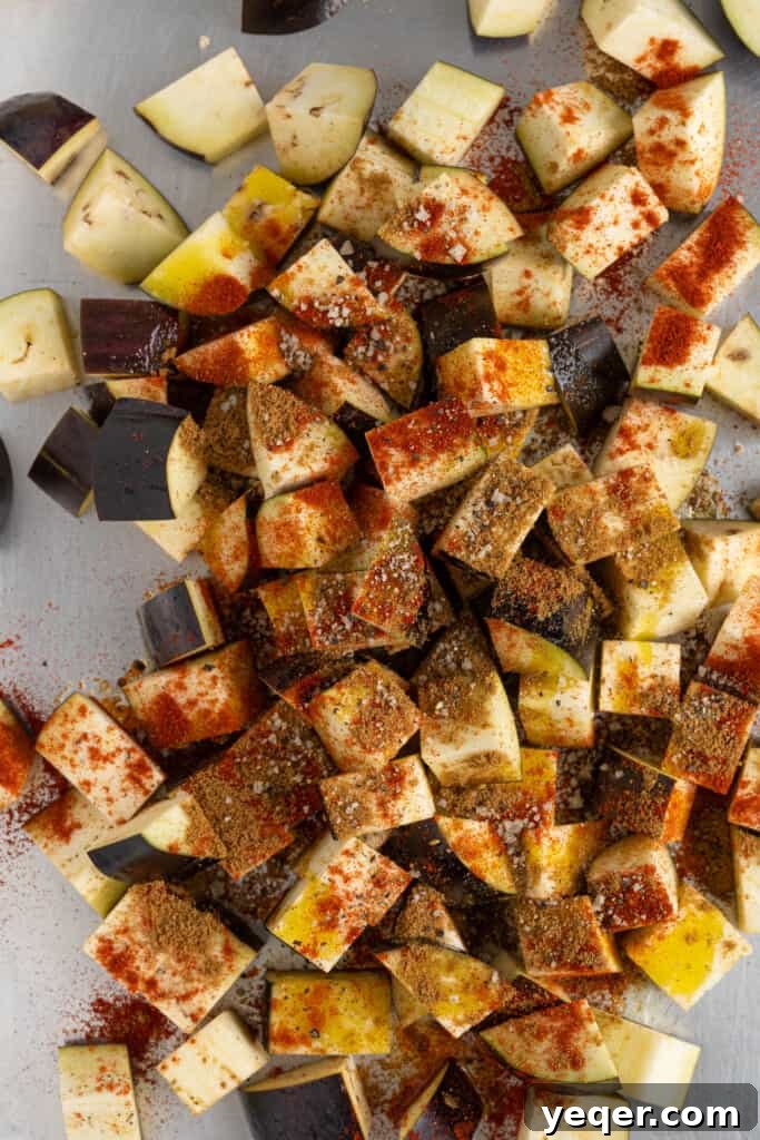 North African Roasted Aubergine in Minutes 4 Eggplant cubes generously coated with olive oil and a vibrant blend of Moroccan spices, including paprika, cumin, salt, and pepper, on a baking sheet.