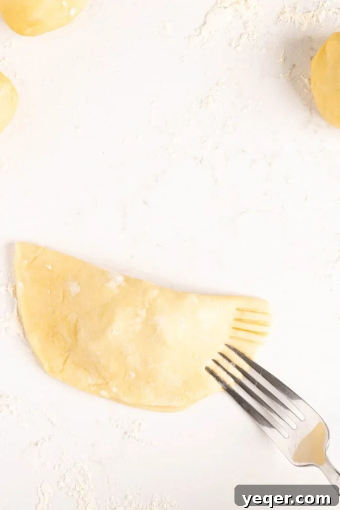 Five-Ingredient Wonder Empanada Dough 13 A close-up view of a fork expertly crimping the edges of an empanada, sealing the filling inside and creating a decorative pattern.