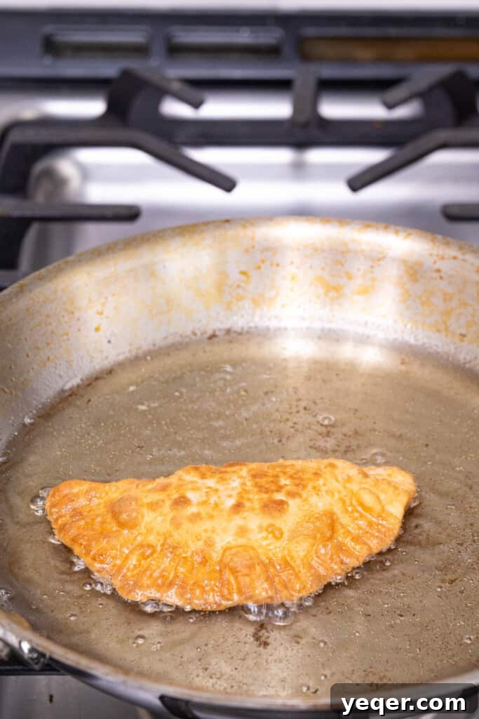 Five-Ingredient Wonder Empanada Dough 14 A golden-brown empanada sizzling beautifully in a shallow pan of hot oil, showcasing the frying process and achieving a perfect crispy exterior.