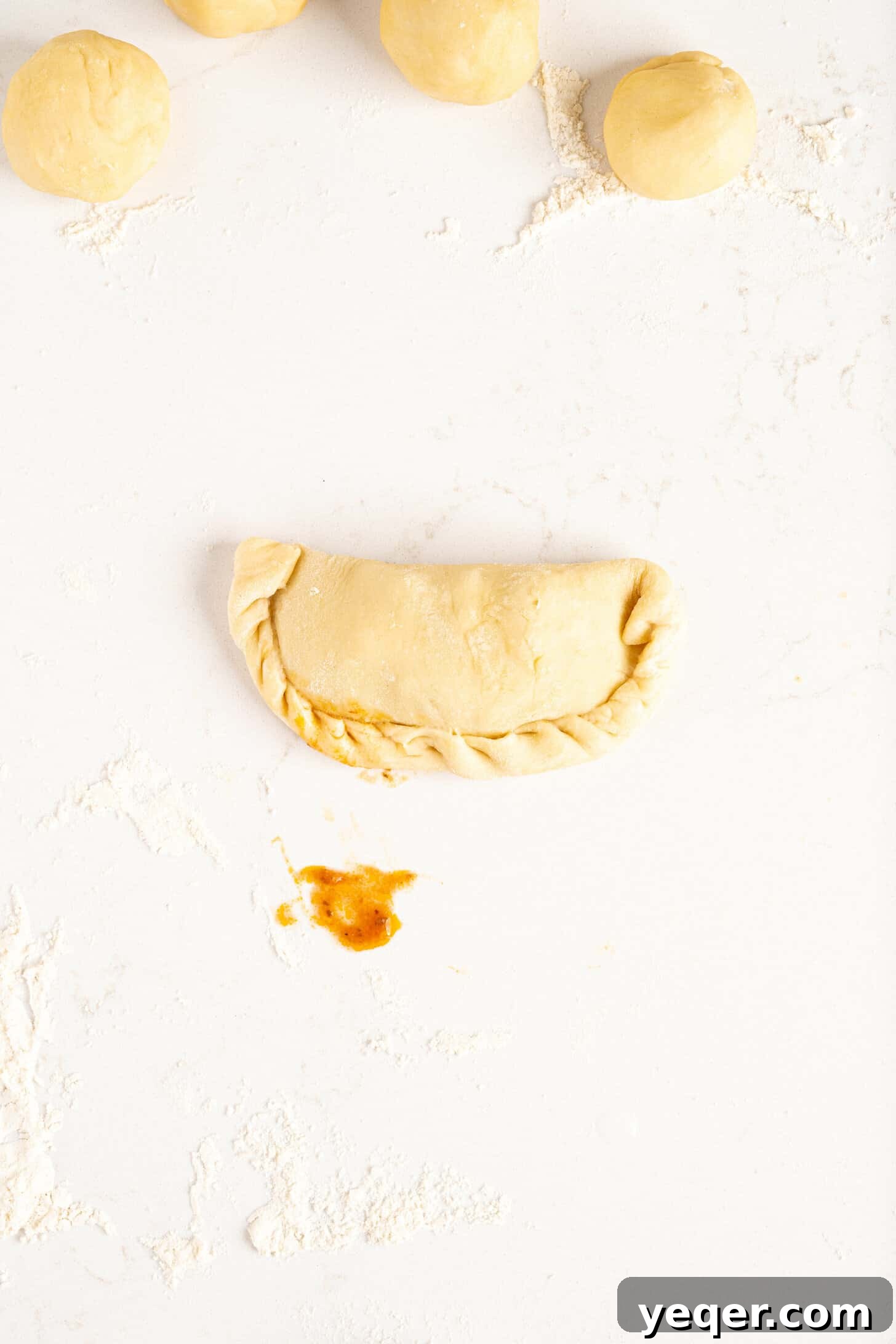 Five-Ingredient Wonder Empanada Dough 16 A perfectly shaped, unbaked empanada with its traditional crimped edges, glistening slightly and ready for cooking.