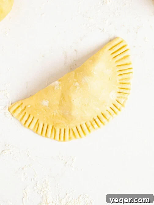 A raw empanada on a white counter, with a floured rolling pin in the background, symbolizing the process of making homemade dough.