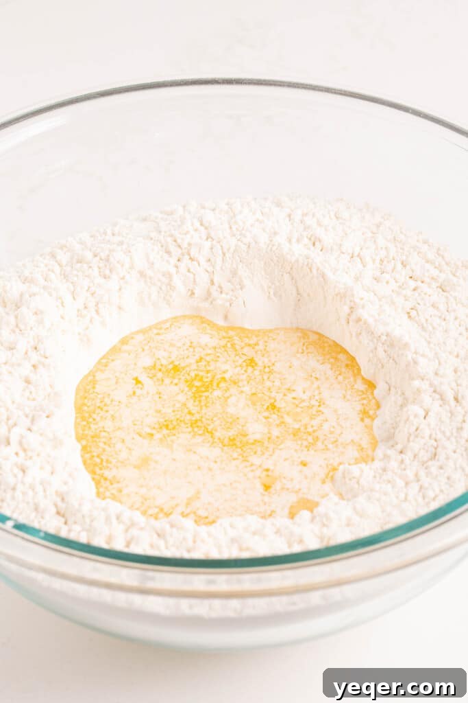 Five-Ingredient Wonder Empanada Dough 6 Melted butter, vibrant egg yolks, and clear water being poured into a bowl of flour, illustrating the addition of wet ingredients to dry.