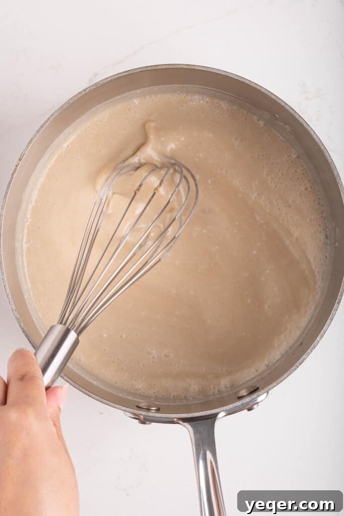 Velvety Vegan Coconut Caramel in 30 Minutes 6 The coconut caramel mixture simmering and thickening in a pot, with a whisk resting in it.