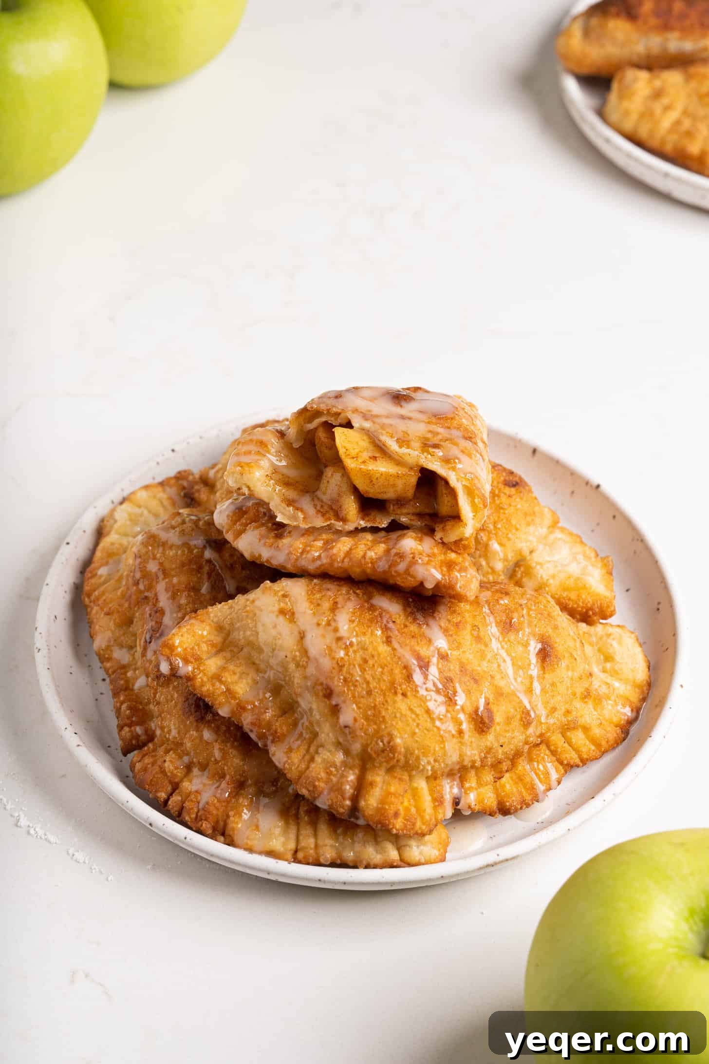 Golden Apple Pastry Pockets 2 Freshly baked apple empanadas on a rustic plate, drizzled with sweet icing.