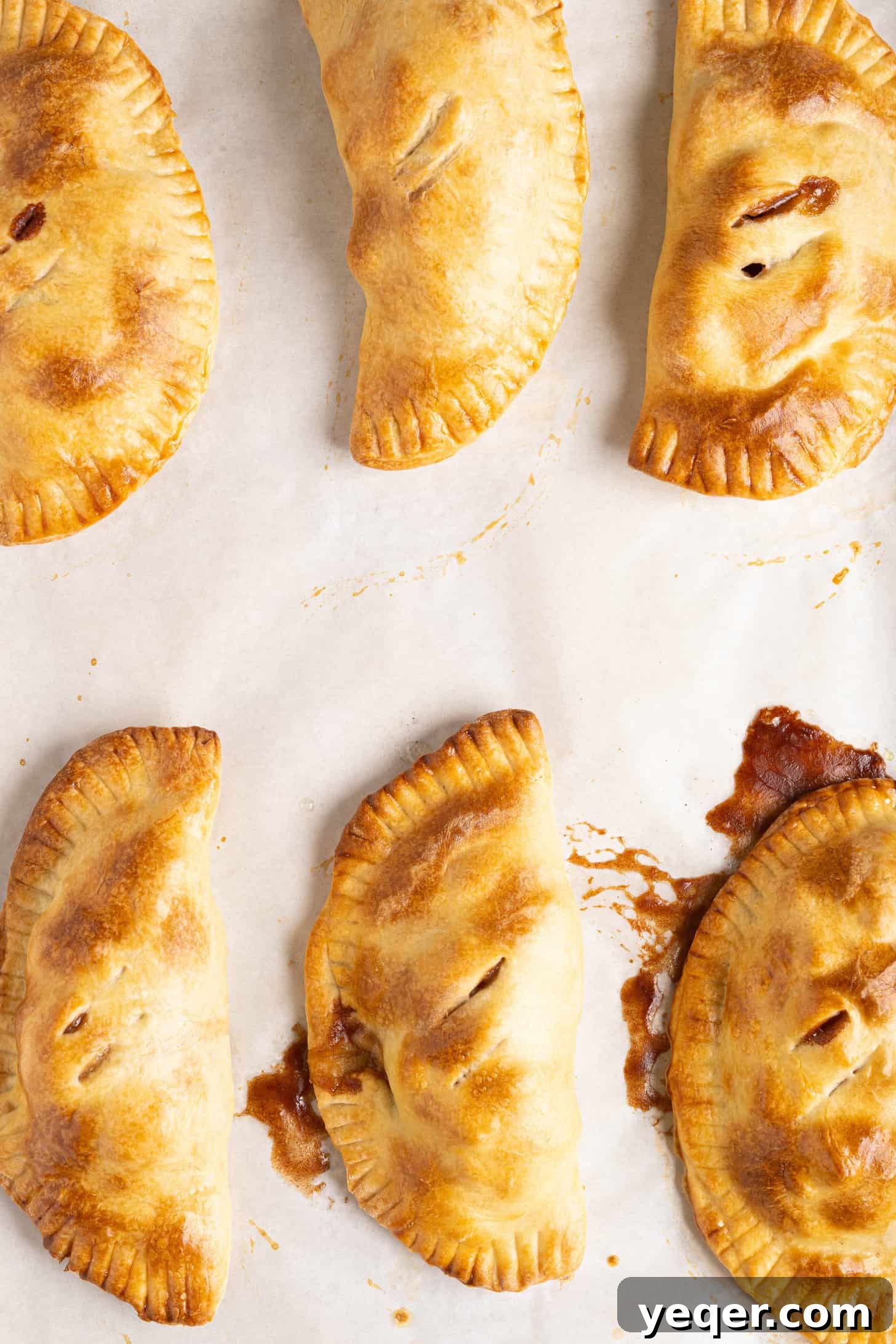 Golden Apple Pastry Pockets 11 A batch of baked apple empanadas, golden and inviting, cooling on a baking sheet.