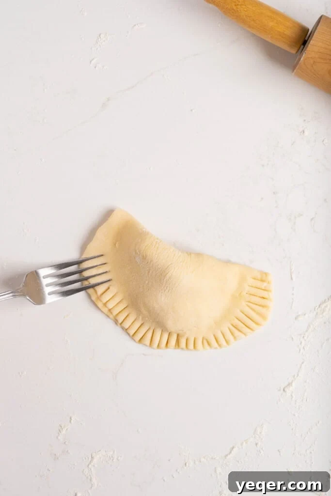 Golden Apple Pastry Pockets 7 A fork pressing the edges of an empanada to create a sealed, decorative crimp.