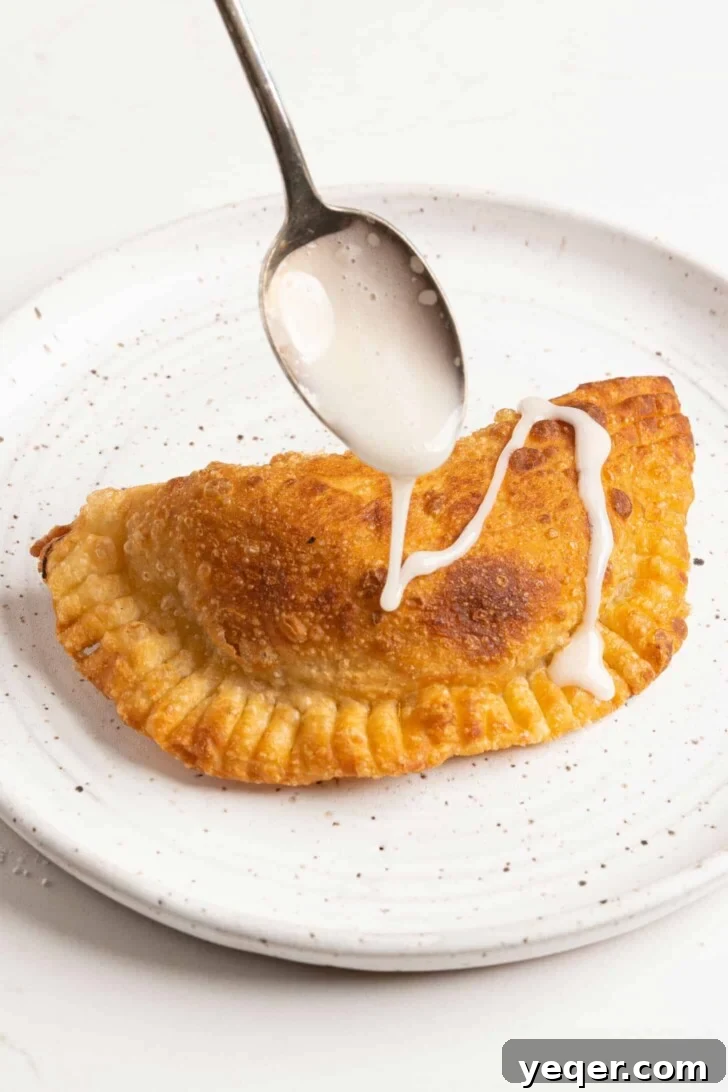 Golden Apple Pastry Pockets 9 Sweet icing being drizzled over warm apple empanadas, creating a delicate pattern.